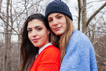 Young attractive happy friends in bright knitted sweaters embracing in forest looking at camera. Winter time, lifestyle concept.