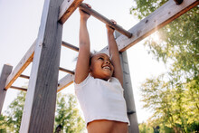 Low Angle View Of Smiling Girl Hanging While Doing Monkey Bars At Summer Camp