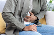 © Tetiana - Close-up photo of the hands of a young Hispanic man in a white t-shirt and shirt holding his stomach. He is sitting on the sofa at home, his body bent over from pain