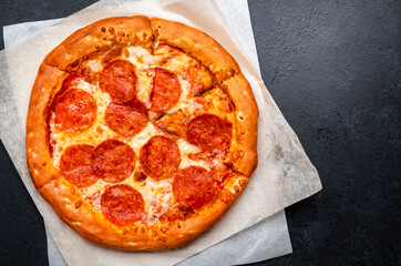 Wall Mural - Hot Pepperoni pizza with salami sausage, cheese, spicy tomato sauce and green basil leaves, ready to eat, black background, top view