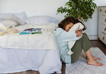 Tired unhappy student teenager sits on the floor in the bedroom. Stress, depression, psychological issue