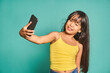 © ADDICTIVE STOCK - Funny ethnic girl child standing with smartphone and taking selfie near turquoise backdrop