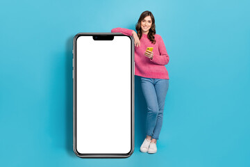 Wall Mural - Full length photo cadre of young charming attractive girl wear pink sweater jeans hold phone huge touchscreen menu isolated on blue color background