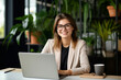 © Tetiana - Photo generative AI portrait of happy charming lady director with brown hair sitting in comfort workplace browsing media on netbook