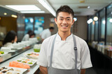 Fototapeta Sypialnia - Portrait of a smiling Japanese waiter in uniform. A chef, an itamae or master sushi chef wearing white jacket and apron in sushi restaurant.