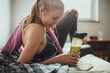 © Geber86 - Young athletic and fit woman using a smartphone while drinking a healthy smoothie or shake after working out and exercising in the gym