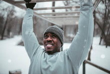 Young African American man doing pull-ups and exercising in an outdoor park during winter and snow