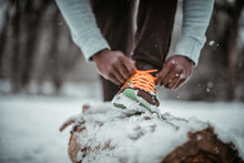 Young African American Man Tying His Shoelaces While Working Out Outdoors During Winter And Snow