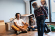 © BalanceFormCreative - Mixed race family moving into their new home. Parents are sitting on the floor while kids dancing.