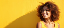 Banner With Close Up Portrait Of Happy, Smiling, Squints From The Sun African Girl With Curly Hair Against Yellow Wall And Copy Space. 