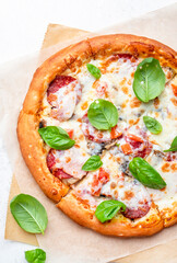 Wall Mural - Homemade pizza with italian salami sausage, mozzarella cheese, tomato sauce and green basil on white kitchen table background, top view