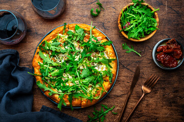 Wall Mural - Hot pizza with mozzarella cheese, ham, pesto sauce and fresh arugula, rustic wooden table background, top view