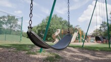 Handheld Slow Motion View Of Single Empty Swing Set With Chains Hanging At Recreational Children's Playground At Public Park With No Swinging