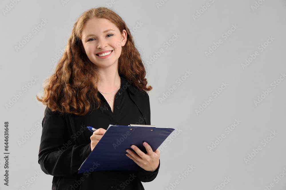 Young businesswoman with clipboard on light background