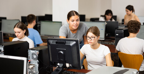 Wall Mural - Schoolgirl using computer and teacher helping to him in classroom