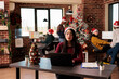 © DC Studio - Asian woman in santa hat working on laptop in decorated office during winter holiday season. Employee using computer at workplace ready for christmas eve celebration party