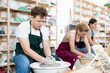 © JackF - Young woman teacher in apron shows students teenage girl and teenage boy how to sculpt ceramic product from raw clay on potter's wheel