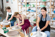 © JackF - Young woman teacher in apron shows students teenage girl and teenage boy how to sculpt ceramic product from raw clay on potter's wheel