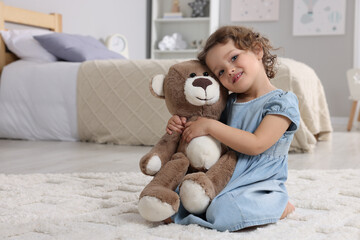 Cute little girl with teddy bear on floor at home