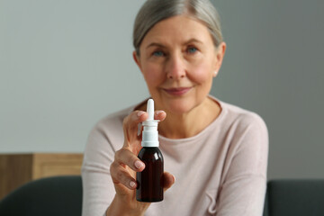 Poster - Woman holding nasal spray indoors, focus on bottle