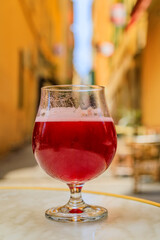 Wall Mural - Glass of a raspberry Lambic ale at an outdoor restaurant with a background of blurred buildings in old town or Vieille Ville in Nice, South of France