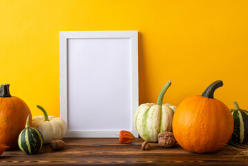 Wall Mural - Thanksgiving Crop Exhibition. Side view picture showcasing empty photo frame and abundant harvest arrangement on rustic wooden table, set against orange wall background, with space for text or advert