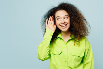 Canvas Print - Young curious nosy latin woman she wear green shirt casual clothes try to hear you overhear listening intently isolated on plain pastel light blue cyan background studio portrait. Lifestyle concept.