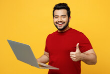 Satisfied Side View Smart Young Happy IT Indian Man Wearing Red T-shirt Casual Clothes Hold Use Work On Laptop Pc Computer Show Thumb Up Isolated On Plain Yellow Orange Background. Lifestyle Concept.