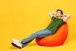 © ViDi Studio - Full body side view young fun happy man he wears green t-shirt casual clothes sit in bag chair hold hands behind neck take nap isolated on plain yellow background studio portrait. Lifestyle concept.