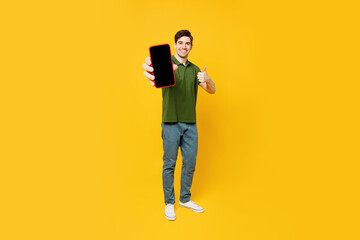 Full body young happy satisfied man he wear green t-shirt casual clothes hold in hand use close up mobile cell phone with blank screen workspace area show thumb up isolated on plain yellow background