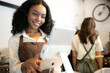© Wosunan - Portrait of smiling waitress using digital tablet in coffee shop with colleagues in background
