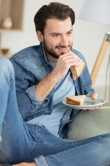 man eating a sandwich sat on the sofa