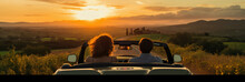 Happy Couple Man And Woman Traveling In Car Italian Tuscan Landscape View Under Sunset Light. Man And Woman Traveler Enjoys Convertible On A Summer Day.
