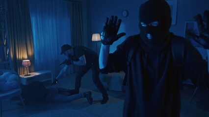 Shot of two burglars, intruders, being caught red-handed in the house. Policeman is pointing a gun at them. Men get on the ground.