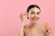 Beautiful young woman applying serum onto her face on pink background. Space for text