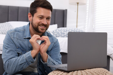 Canvas Print - Happy man making heart with hands during video chat via laptop at home. Long-distance relationship