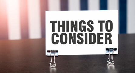 THINGS TO CONSIDER sign on paper on dark desk in sunlight. Blue and white background