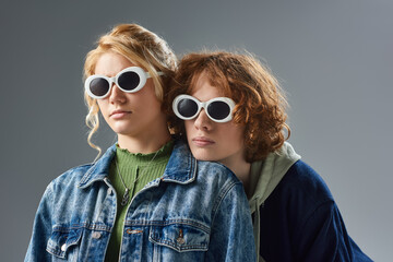 Wall Mural - portrait of redhead teen guy and blonde girlfriend in sunglasses and stylish outfit posing on grey