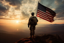 American Soldier Holding A Flag On The Peak Of A Mountain At Sunset. Copy Space For Text