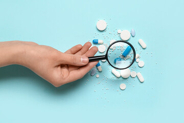 Wall Mural - Female hand with magnifier and pills on blue background