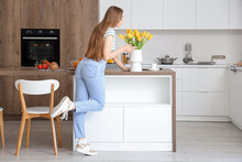 Beautiful Young Woman Smelling Blooming Tulip Flowers In Modern Kitchen
