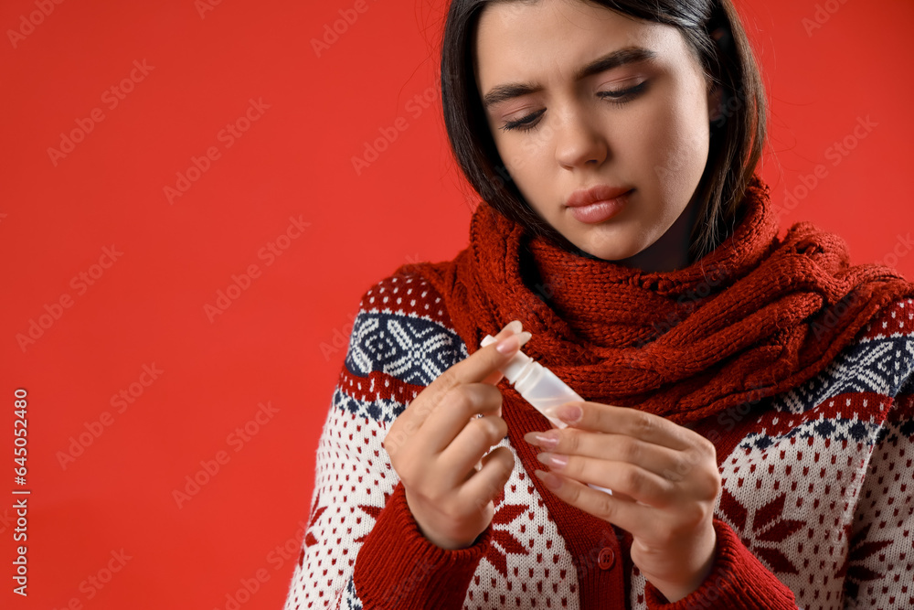 Sick young woman with nasal drops on red background