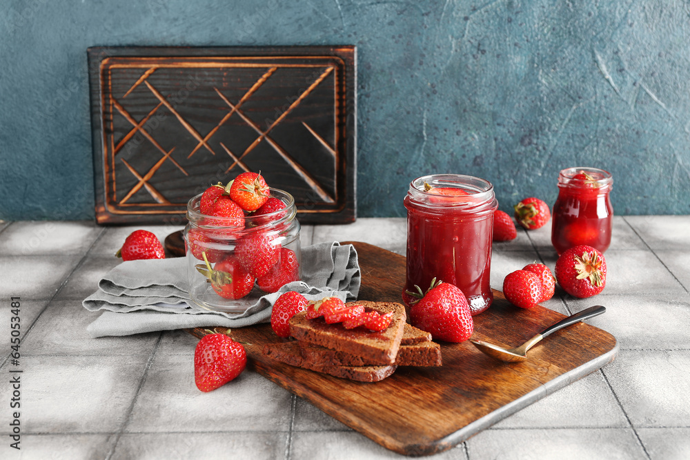 Jars of sweet strawberry jam, fresh berries and bread on table