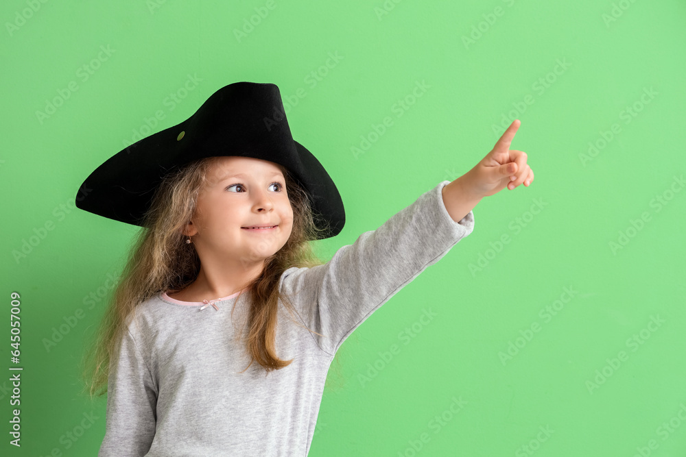 Cute little girl dressed as pirate pointing at something on green background