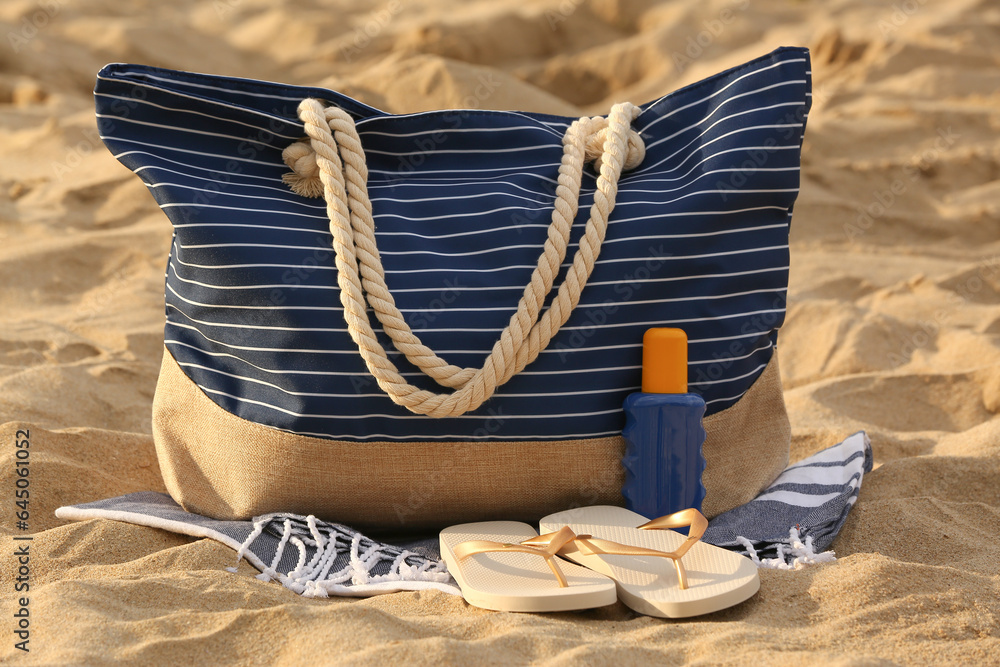 Summer bag with different beach accessories on sand at resort