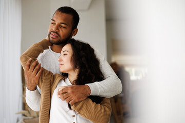 Young african american man embracing brunette asian girlfriend in casual clothes at home