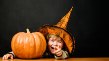 Smiling Child Boy In Witch Hat With Pumpkin. Halloween Holidays. Cute Kid With Halloween Pumpkin. Autumn Recipes. Thanksgiving Day Cooking. Halloween Preparation. Useful Vegetables. Traditional Food.