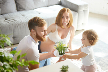 Wall Mural - Beautiful young couple, parents spending time with little girl, daughter at home. Woman expecting baby. Concept of pregnancy, family, love, relationship, parenthood and childhood