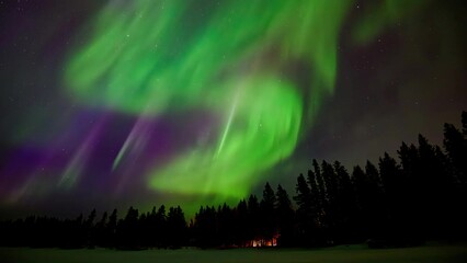 spectacular green to purple aurora in a star filled sky above an evergreen forest with fire light sh