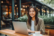© VisualProduction - Beautiful smiley young female chinese office assistant working remotely on her computer outside the coffee shop